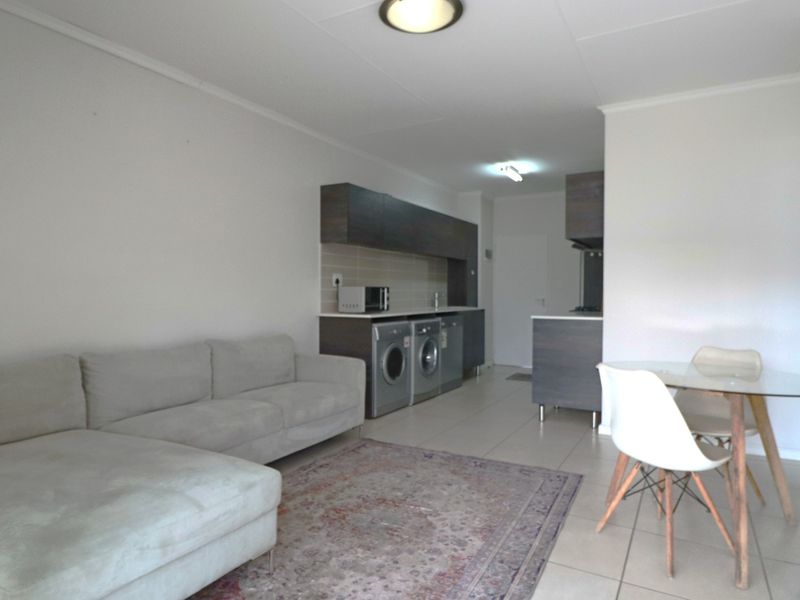Open-plan living area featuring tiled floors, a compact kitchen with built-in cabinetry, and integrated laundry facilities.