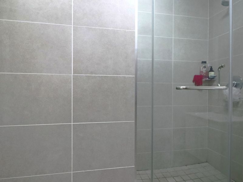 A modern bathroom featuring a walk-in shower with a glass screen and neutral grey ceramic wall tiling.