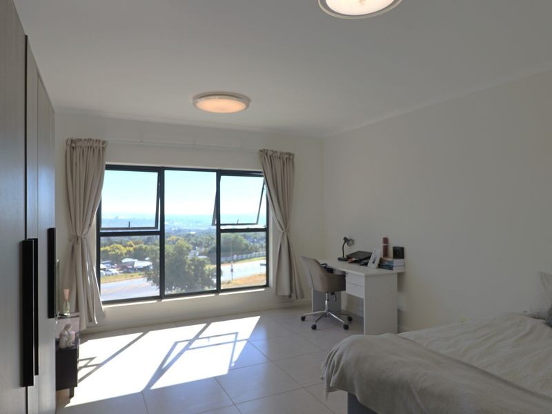 Bright bedroom featuring tiled flooring, built-in wardrobes, and large windows offering expansive elevated views.