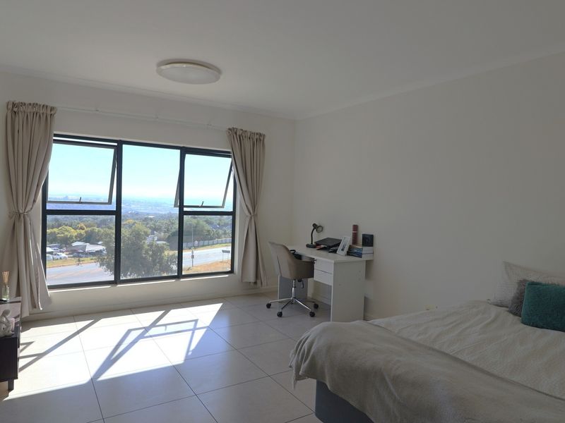A bright bedroom featuring tiled flooring, a built-in cupboard, and a large window offering expansive views.