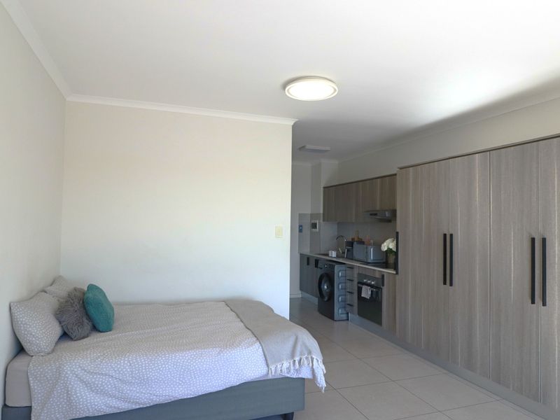 Open-plan studio apartment featuring a modern kitchenette with built-in cabinetry, integrated appliances, and tiled flooring throughout.