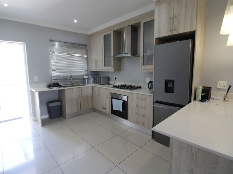 Modern kitchen featuring light wood-grain cabinetry, stone countertops, integrated gas hob, built-in oven, stainless steel extractor fan, and tiled flooring with direct outdoor access.