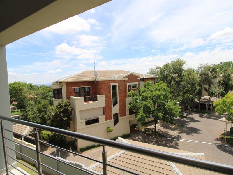 Elevated view from a balcony overlooking the apartment complex grounds, featuring brick architecture and mature trees.