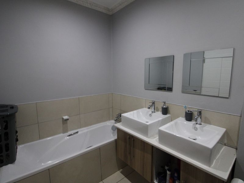 A functional bathroom featuring a double vanity with modern vessel sinks, a built-in bathtub, and neutral wall tiling.