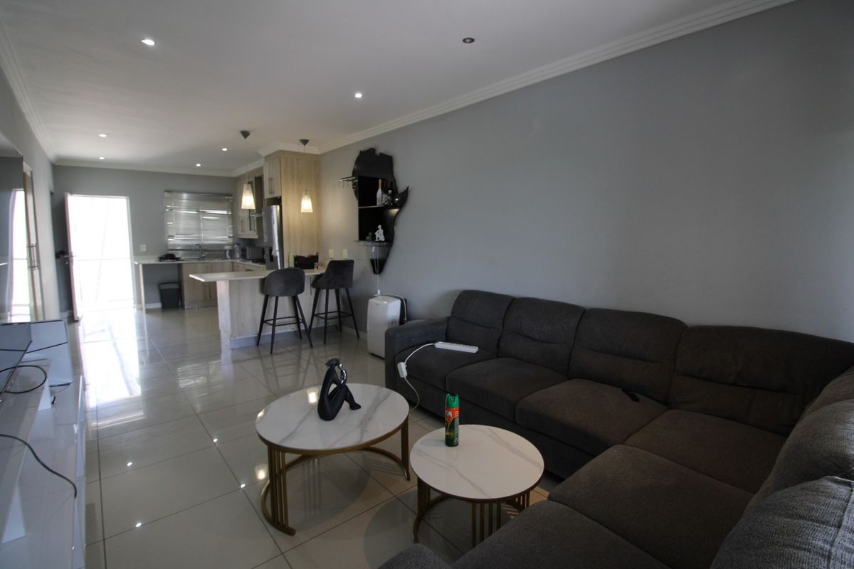 An open-plan living and kitchen area featuring modern porcelain floor tiles, recessed downlighting, and a functional breakfast bar layout.