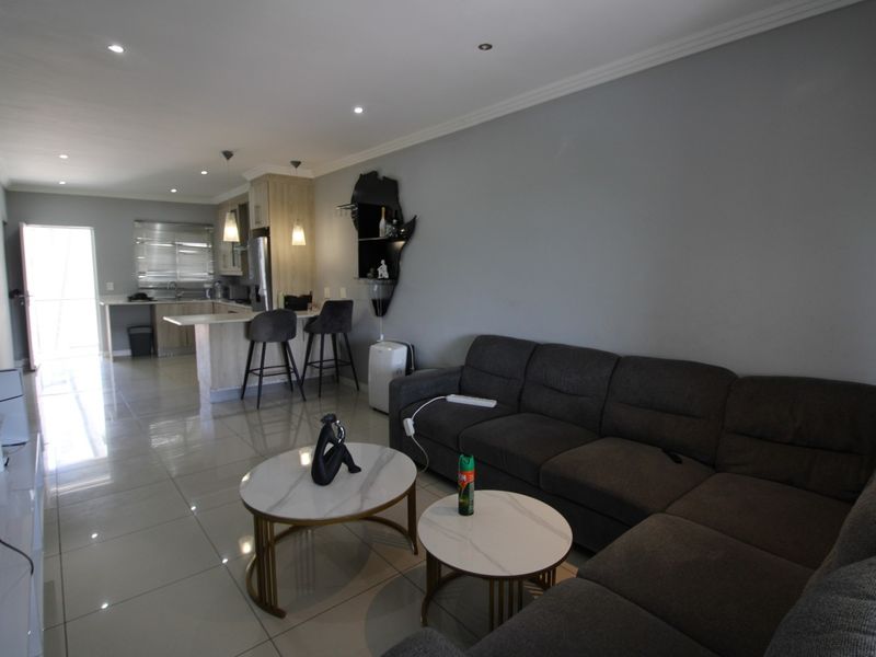 An open-plan living and kitchen area featuring modern porcelain floor tiles, recessed downlighting, and a functional breakfast bar layout.
