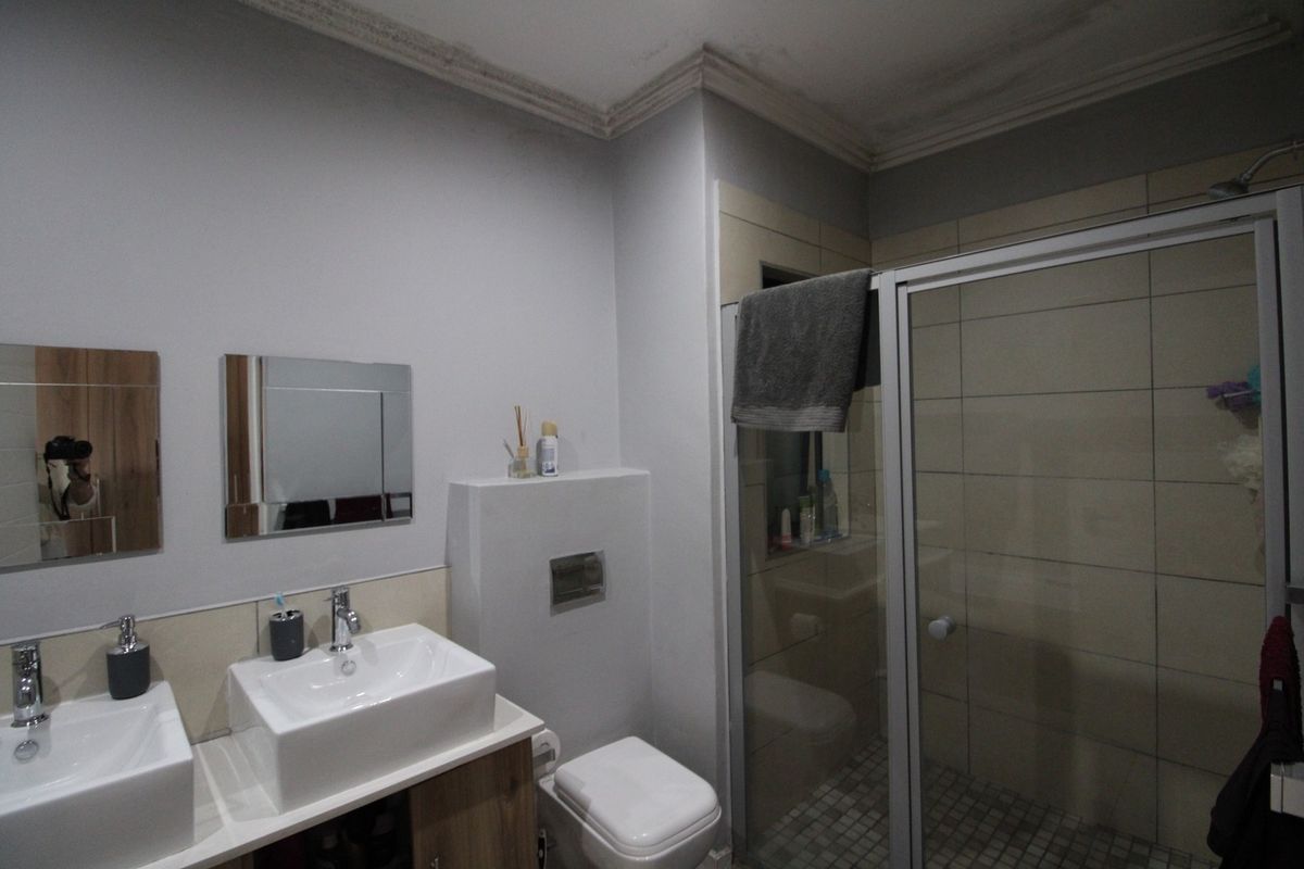 A functional bathroom featuring a double vanity with vessel sinks, a wall-mounted toilet, and a glass-enclosed shower with tiled walls.