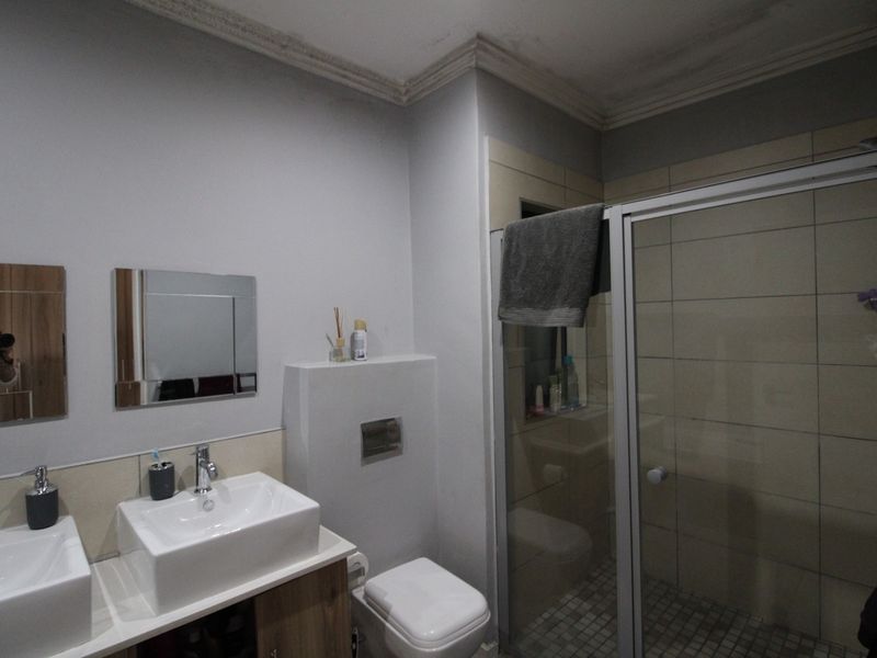 A functional bathroom featuring a double vanity with vessel sinks, a wall-mounted toilet, and a glass-enclosed shower with tiled walls.