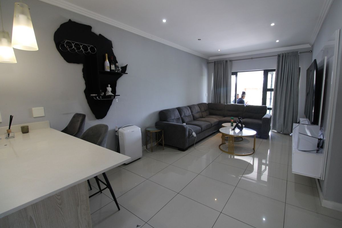 Modern open-plan living area featuring polished porcelain floor tiles, recessed downlighting, and a functional kitchen island, seamlessly connecting to an outdoor balcony.