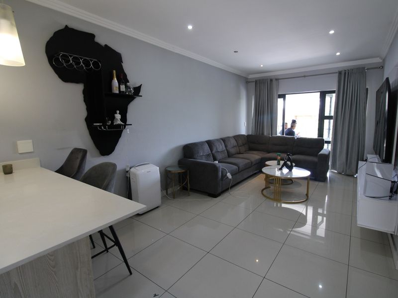 Modern open-plan living area featuring polished porcelain floor tiles, recessed downlighting, and a functional kitchen island, seamlessly connecting to an outdoor balcony.