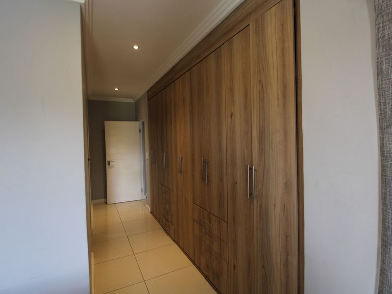 A well-maintained hallway featuring extensive built-in wooden cabinetry, tiled flooring, and recessed downlighting.