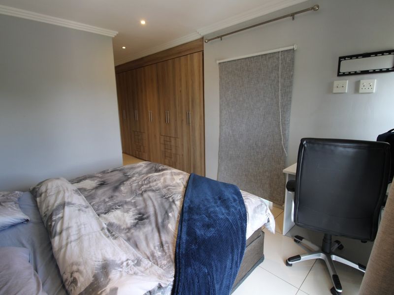 A well-maintained bedroom featuring built-in wooden cupboards, tiled flooring, and recessed lighting, offering a clean and functional living space.