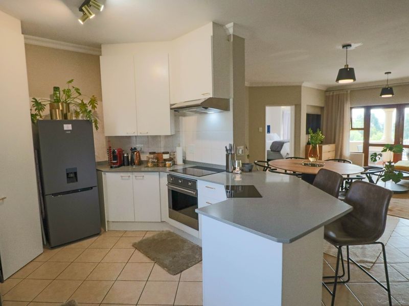 Open-plan kitchen featuring white cabinetry, stone countertops, and integrated appliances, flowing seamlessly into the dining and living area with tiled flooring throughout.