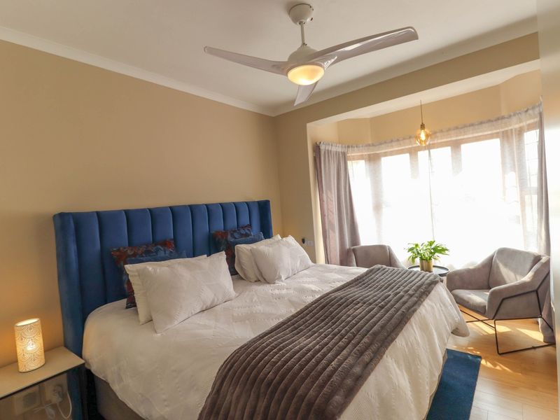 A well-lit bedroom featuring a bay window, ceiling fan, and laminate flooring, offering a comfortable and inviting living space.