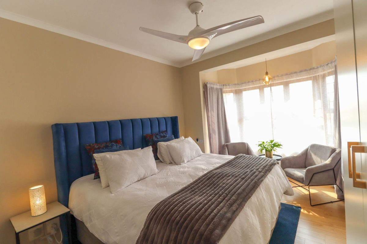 A well-lit bedroom featuring a bay window, ceiling fan, and laminate flooring, offering a comfortable and inviting living space.