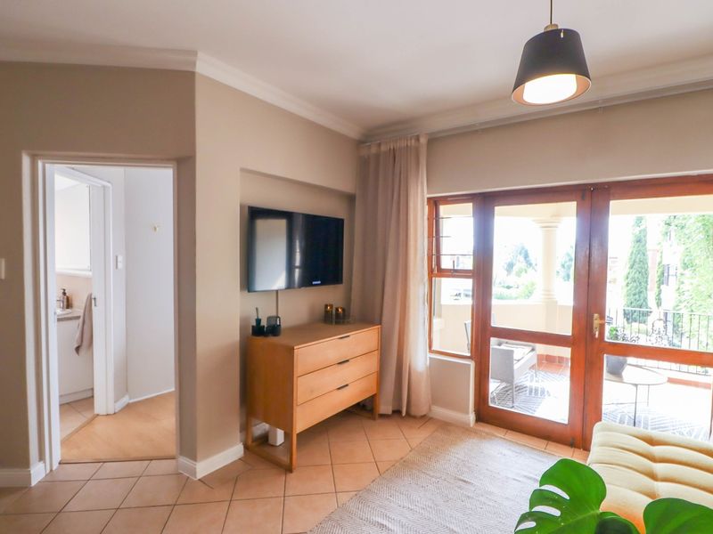 A bright living room featuring tiled floors, neutral walls, and direct access to an outdoor balcony through a wooden framed door.
