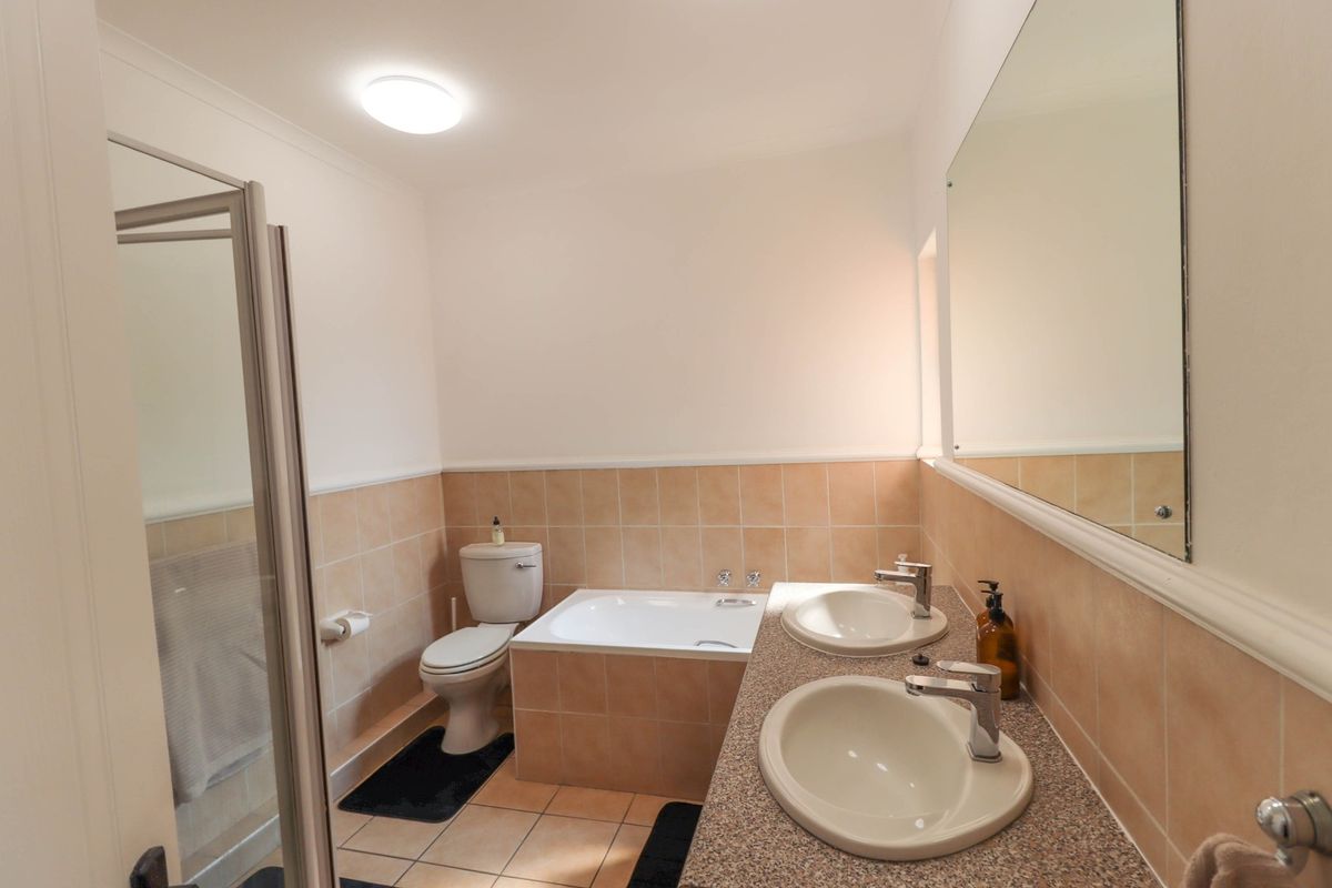A functional bathroom featuring a dual vanity, built-in bathtub, and a separate shower enclosure with neutral wall and floor tiling.