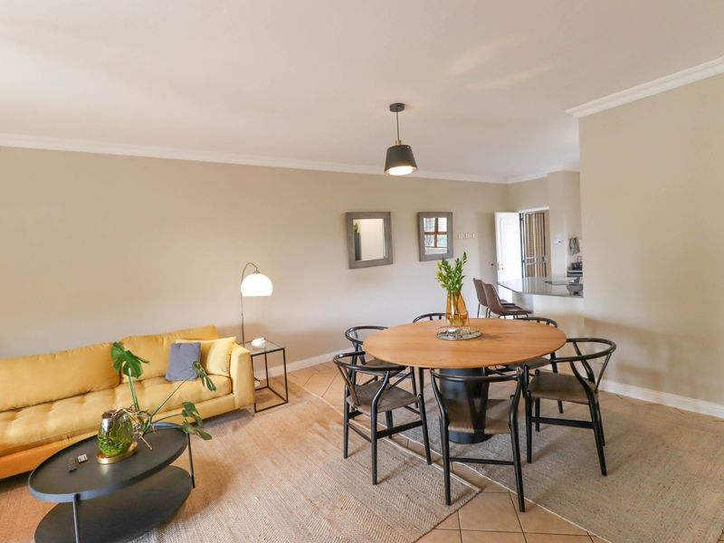 An open-plan living and dining area featuring tiled flooring, neutral walls, and a breakfast bar connecting to the kitchen space.