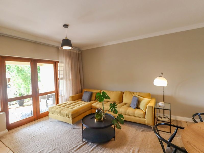 A bright living room featuring tiled flooring, cove cornicing, and wooden framed glass sliding doors providing access to an outdoor patio area.