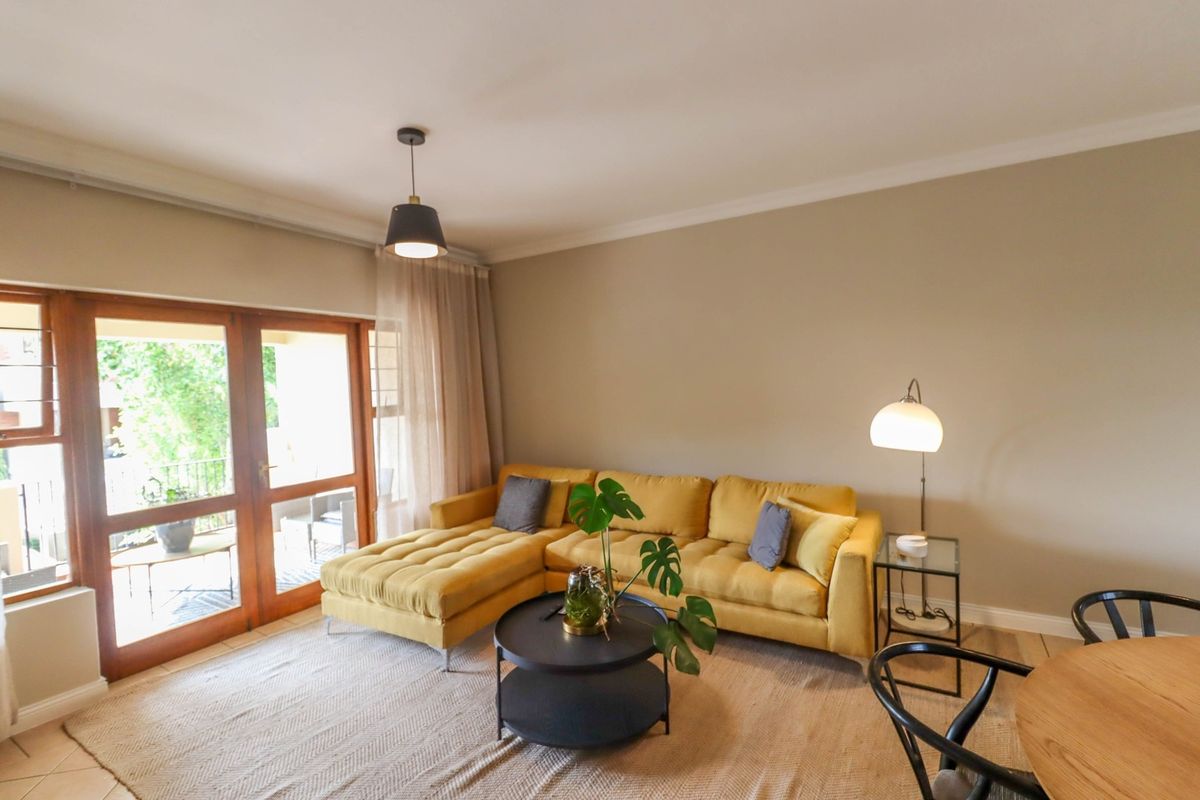 A bright living room featuring tiled flooring, cove cornicing, and wooden framed glass sliding doors providing access to an outdoor patio area.