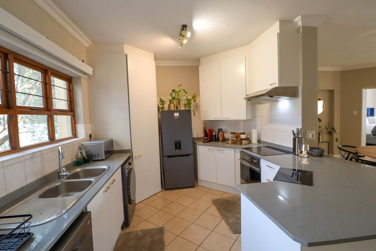 A functional kitchen featuring white cabinetry, quartz countertops, a double bowl sink, built-in oven, and electric hob with an extractor fan.