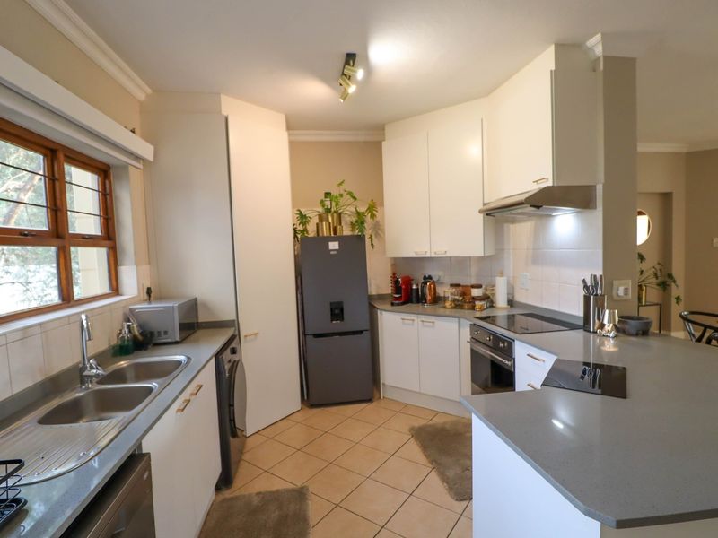 A functional kitchen featuring white cabinetry, quartz countertops, a double bowl sink, built-in oven, and electric hob with an extractor fan.