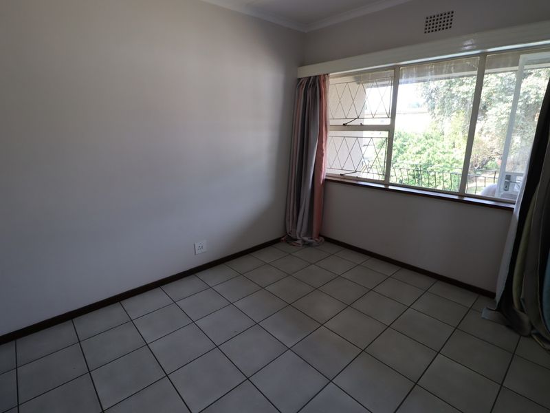 A vacant bedroom featuring neutral wall finishes, tiled flooring, and a large window with security bars, offering a blank canvas for personalization.