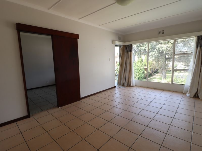A spacious, empty living area featuring neutral tiled flooring, a large window providing natural light, and a sliding door leading to an adjacent room.