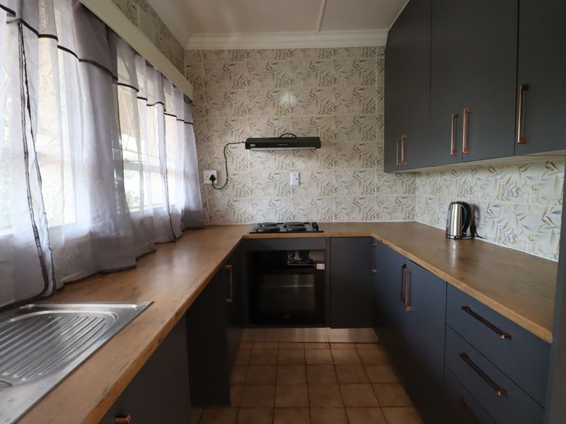 A functional kitchen featuring dark cabinetry, wooden countertops, a built-in oven with gas hob, and a tiled backsplash.