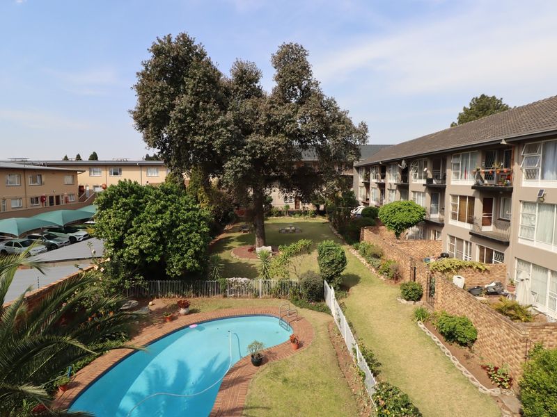 Aerial view of the apartment complex featuring a communal swimming pool, landscaped garden areas, and covered parking facilities.