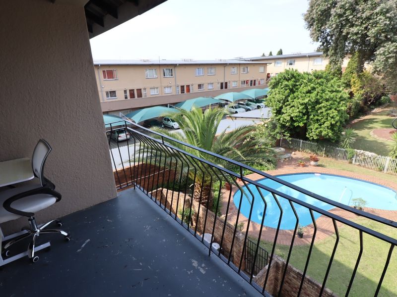 A private balcony overlooking the complex swimming pool, garden area, and covered parking bays.