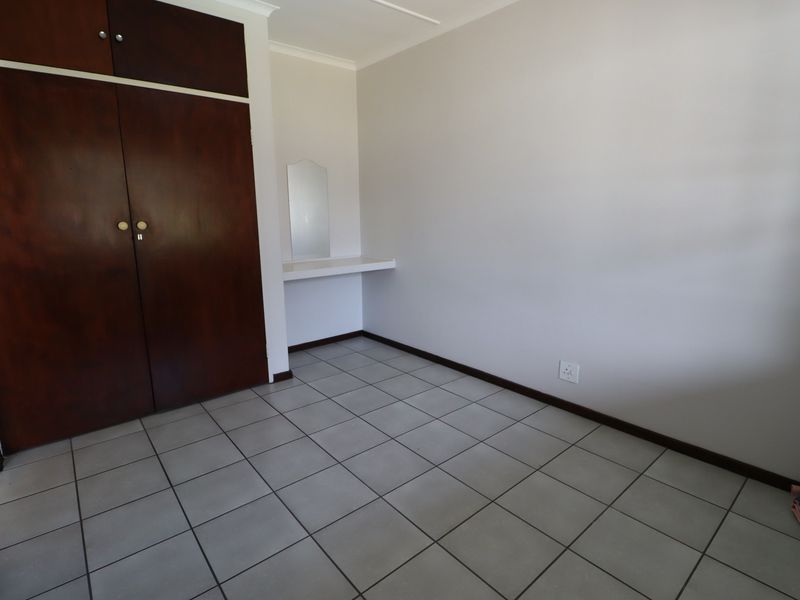 A clean, empty bedroom featuring neutral tiled flooring, built-in wooden cupboards, and a small integrated vanity area.