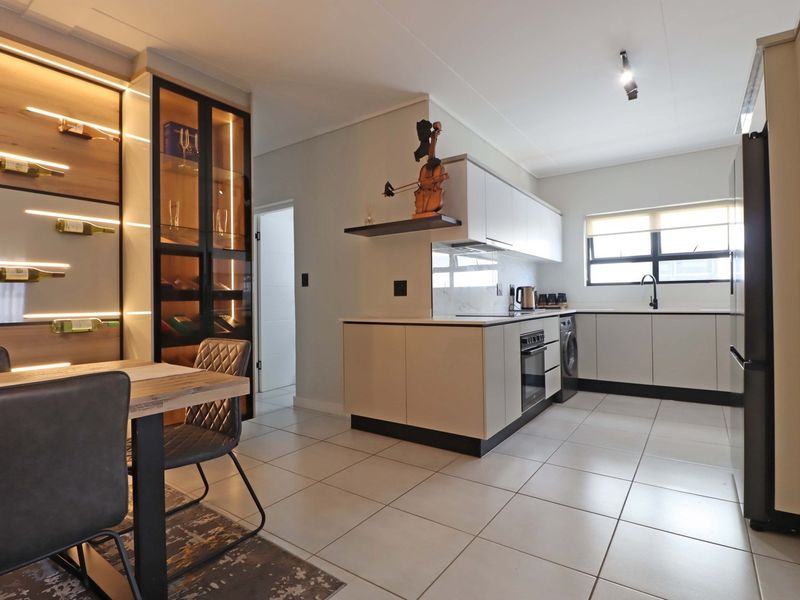 Modern kitchen featuring sleek cabinetry, integrated wine storage with ambient lighting, built-in appliances, and high-quality tiled flooring in an open-plan layout.