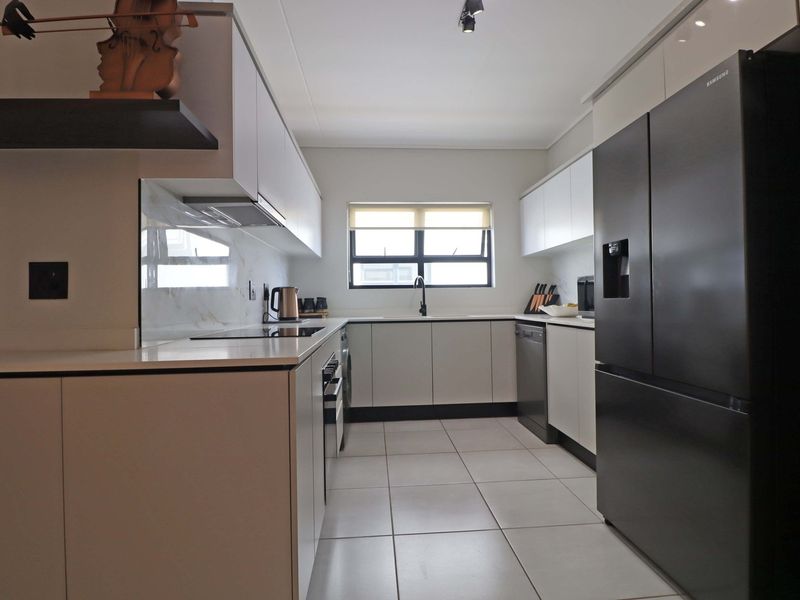 Modern galley-style kitchen featuring sleek white cabinetry, marble-look splashbacks, stone countertops, and high-quality integrated appliances with neutral tiled flooring.