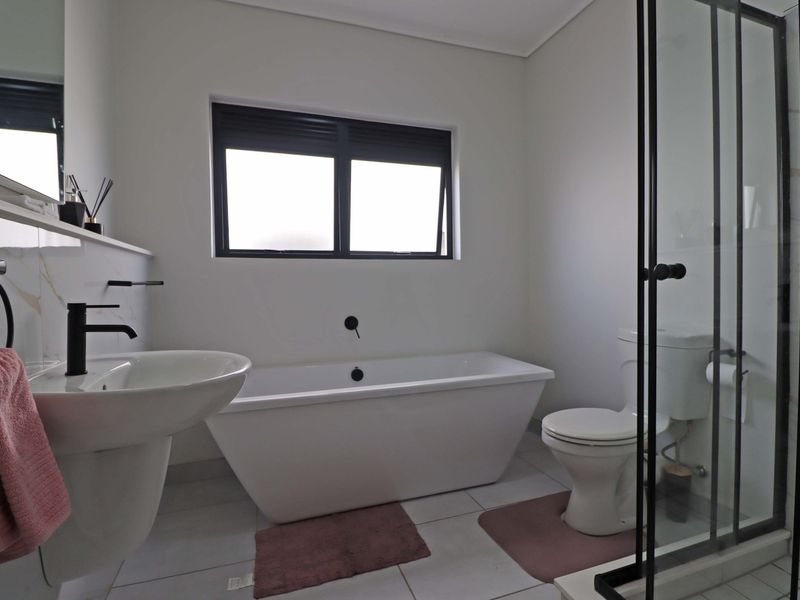 Modern bathroom featuring a freestanding bathtub, separate shower enclosure, pedestal sink, and contemporary black fixtures with neutral floor tiling.