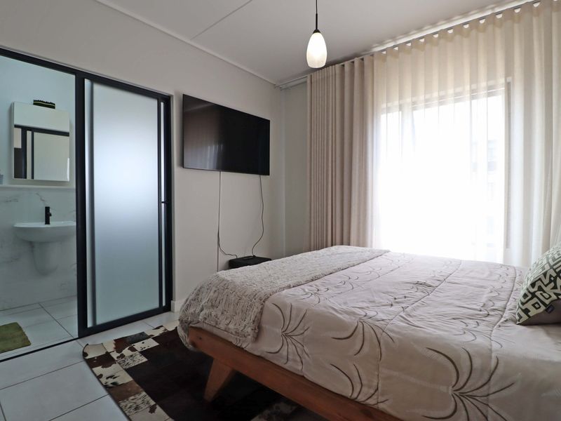 A well-maintained bedroom featuring an en-suite bathroom with a modern frosted glass sliding door, tiled floors, and neutral finishes.