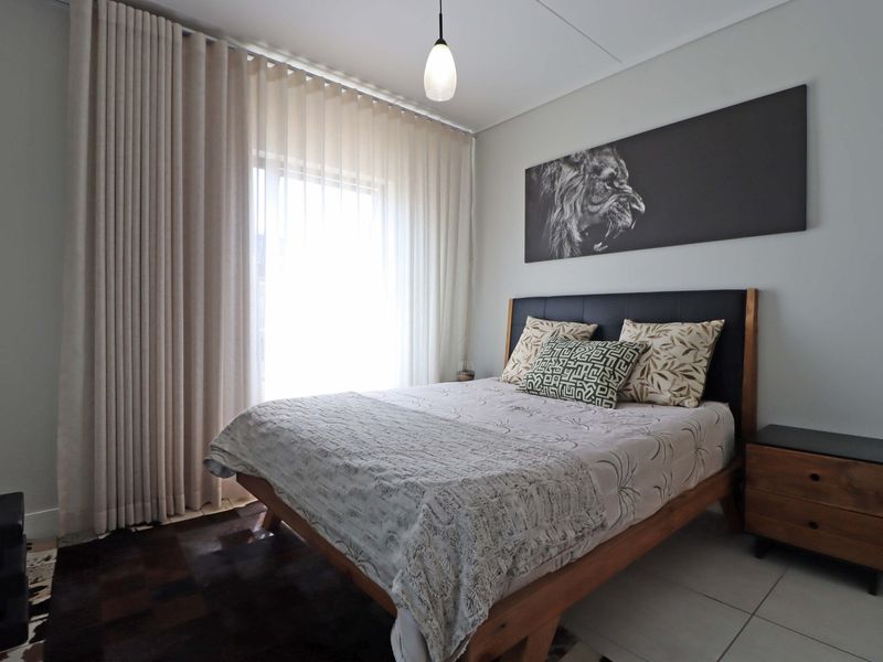 A well-maintained bedroom featuring neutral tiled flooring, modern pendant lighting, and floor-to-ceiling curtains providing ample natural light.