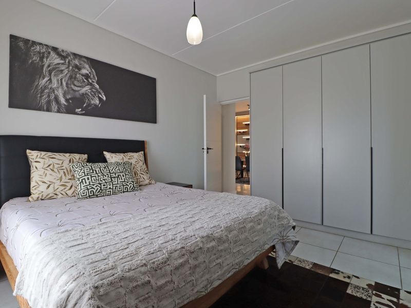 A well-maintained bedroom featuring neutral tiled flooring, ample built-in cupboard storage, and a modern pendant light fixture.