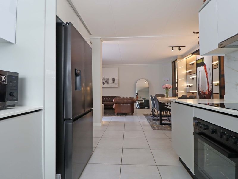 Modern open-plan kitchen and living area featuring sleek cabinetry, integrated appliances, tiled flooring, and contemporary lighting throughout the spacious layout.