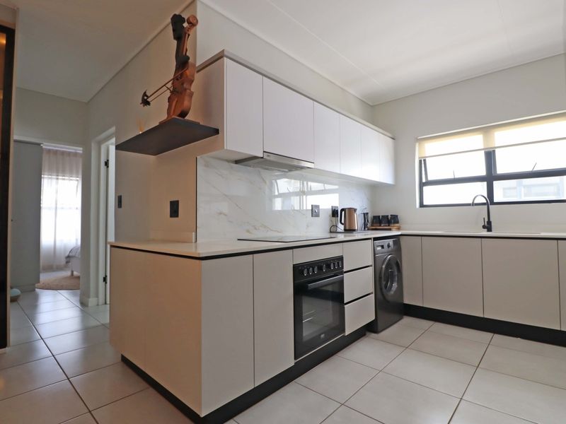 Modern kitchen featuring sleek white cabinetry, marble-look splashback, integrated appliances, and tiled flooring, offering a clean and contemporary aesthetic.