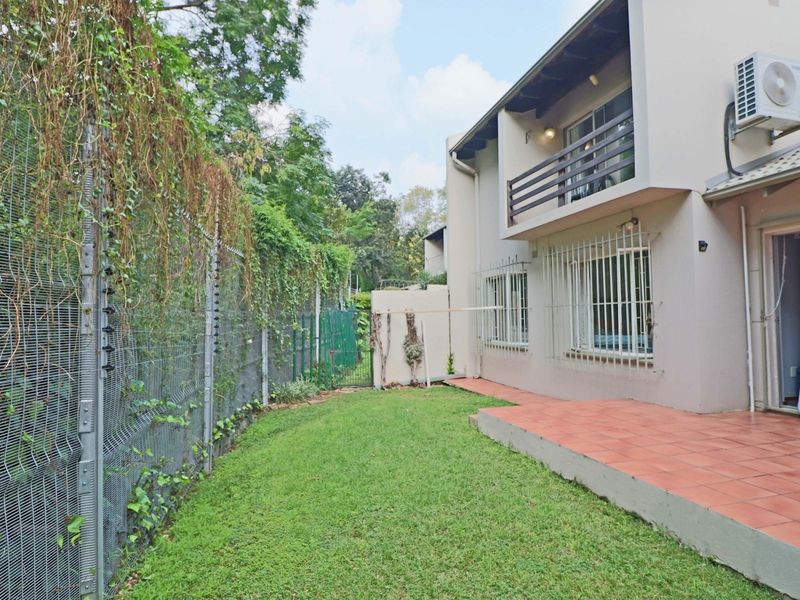 Rear exterior view of the townhouse featuring a tiled patio, small lawn, balcony, and perimeter electric fencing.
