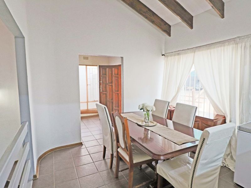 Dining area featuring exposed timber ceiling beams, tiled flooring, and access to an adjacent room through a timber door.