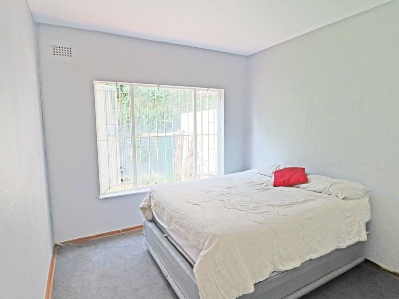 A simple bedroom featuring a window with security bars and grey carpeting, offering a functional space ready for cosmetic updates.