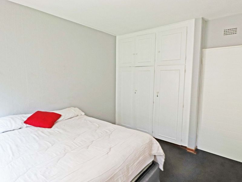 A bedroom featuring neutral walls, dark carpeting, and white built-in cupboards providing ample storage space.