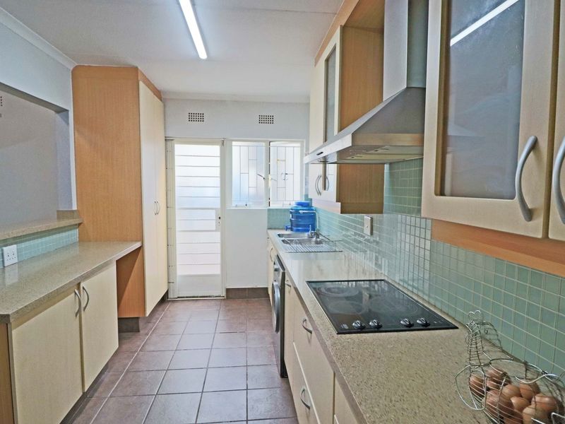 Functional kitchen featuring built-in cabinetry, stone countertops, an electric hob with extractor fan, and tiled flooring with direct access to the exterior.