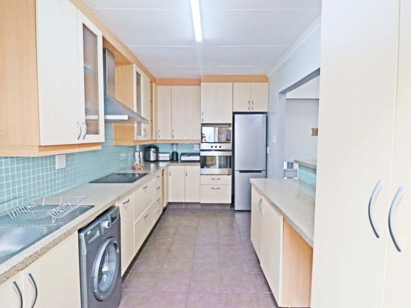 Functional kitchen featuring light-toned cabinetry, mosaic tile backsplash, built-in oven and hob, and tiled flooring with a practical layout.