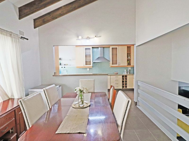 Open plan dining area featuring exposed timber ceiling beams and a pass-through window connecting to a functional kitchen with built-in cabinetry.