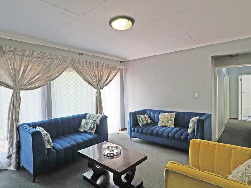 A comfortable living room featuring carpeted flooring, a central ceiling light, and a large sliding glass door providing natural light.