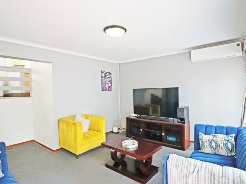 A living room featuring a wall-mounted air conditioning unit, neutral wall finishes, and access to an adjacent staircase.