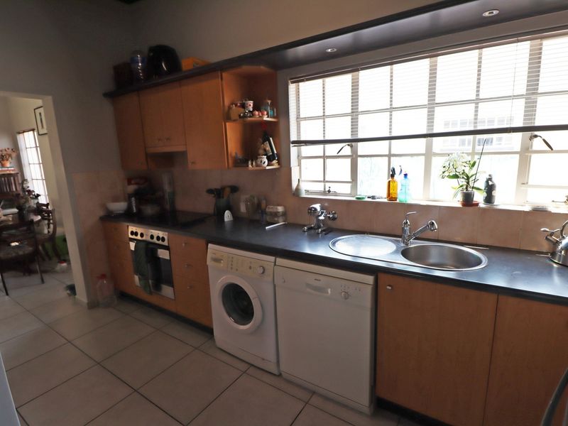 A functional kitchen featuring wooden cabinetry, dark laminate countertops, a stainless steel sink, and integrated appliances, with tiled flooring and a large window.